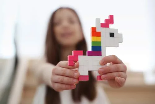 Avante, LEGO blocos formam um unicórnio pixelado branco, rosa e arco-íris nas mãos de uma criança.