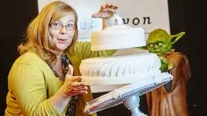 Bolo do Mestre Yoda levitando pela Força: bolo branco de três andares com camadas flutuantes, e figura de Yoda.