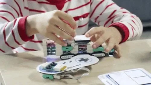 Brinquedo magnético ensina programação para crianças. Mãos infantis montam blocos coloridos e uma placa eletrônica.