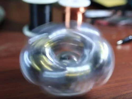 Brinquedo nanodot gyro com ímãs de neodímio girando dentro de invólucro transparente, sobre mesa de madeira.