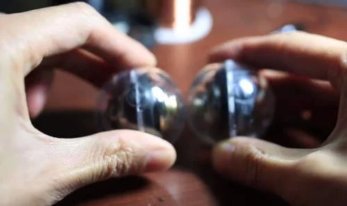 Brinquedo nanodot gyro com ímãs de neodímio: duas esferas metálicas prateadas sendo seguras por mãos, lado a lado.