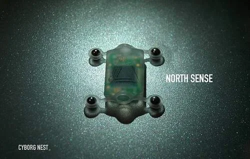 Mini bússola implantável North Sense da Cyborg Nest: dispositivo eletrônico transparente com 4 contatos em superfície escura.