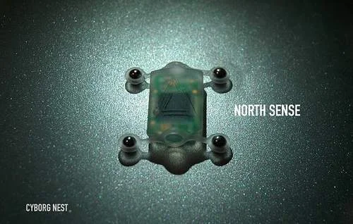 Bússola que pode ser implantada no corpo humano: dispositivo eletrônico transparente, retangular, com placa verde e 4 esferas nas pontas.