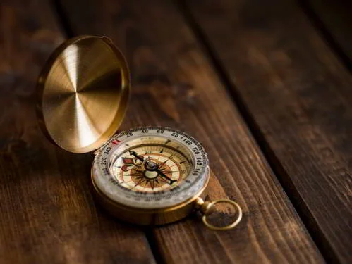 Bússola de latão dourado aberta, a agulha apontando claramente para o norte geográfico, sobre uma superfície de madeira escura.