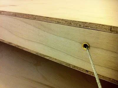 Cama flutuante magnética: detalhe do cabo de aço em ilhós dourado na lateral de madeira compensada.