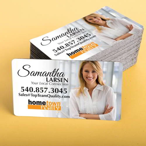 Cartão de visita magnético com foto de mulher sorrindo, detalhes de contato e logo Hometown Realty, com pilha de cartões atrás.
