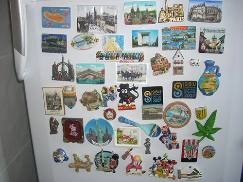 Colecionando ímãs de geladeira: vasta coleção de souvenires turísticos coloridos e variados em porta branca.