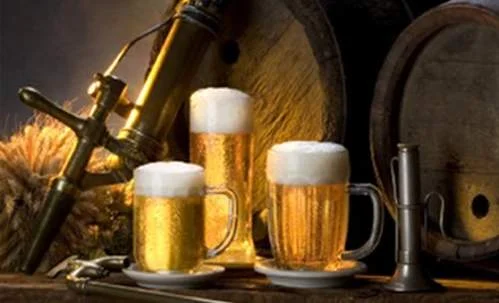 Cerveja clara em canecas com espuma, torneira, trigo e barril de madeira, sugerindo sabor.