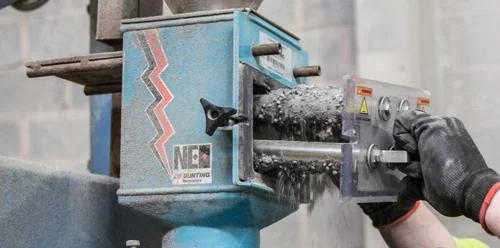 Máquina Bunting com separadores magnéticos ecovyn, operada por mão enluvada, processando material granulado e caindo pó.