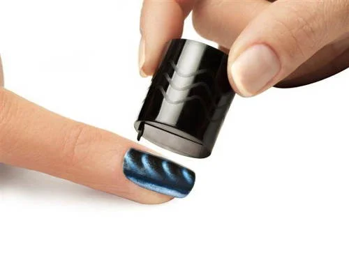 Esmalte magnético azul metálico com padrões ondulados na unha, sendo ativado por ímã cilíndrico preto.
