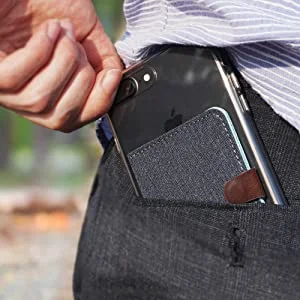 Smartphone preto com fecho frontal magnético (porta-cartões cinza) sendo guardado no bolso da calça.