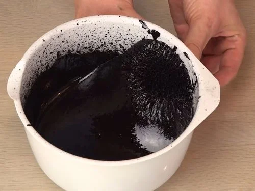 Ferropast, o ferrofluido caseiro preto em tigela branca, exibindo espículas magnéticas na superfície. Uma mão segura o recipiente.