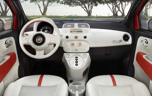 Interior do Fiat 500e. Painel e volante brancos, assentos brancos com faixa vermelha, logo Fiat no volante.