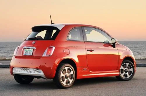 Fiat 500e vermelho elétrico, visão traseira, estacionado à beira-mar com pôr do sol.