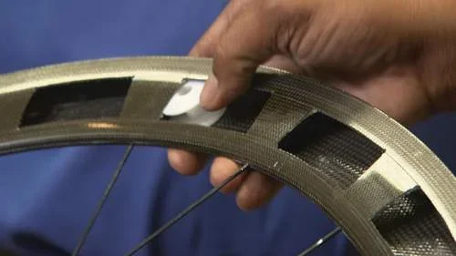 Ímã branco plano sendo inserido por mão em abertura de aro de bicicleta de carbono. Ímãs escondidos para fraude no ciclismo.