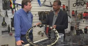 Fraude no ciclismo por ímãs escondidos: Dois homens em loja inspecionam roda de bicicleta com cassete.