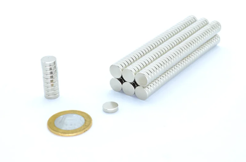 Ímãs de neodímio 10x3mm prateados: um empilhado, um solto e vários em fileiras. Moeda para escala.