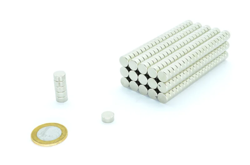 Ímã de neodímio 10x5mm. Bloco de ímãs cilíndricos prateados empilhados, mais uma pilha e um ímã solto com moeda de 1 Real.