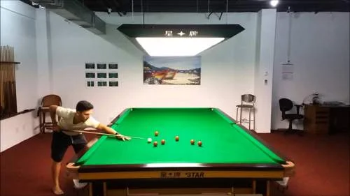 Homem joga bilhar, inclinando-se sobre uma mesa de bilhar verde com bolas e taco.