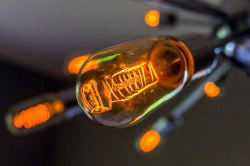 Lâmpada incandescente acesa com filamento espiralado laranja, mostrando como calor transforma em energia.