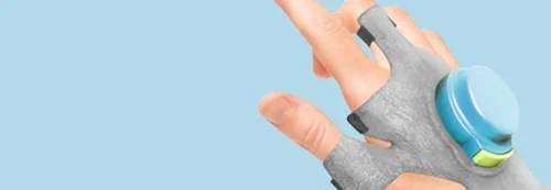 Luva cinza para controlar tremores de Parkinson, com módulo azul circular e botão verde na parte superior da mão.