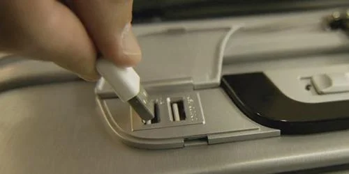 Malas com GPS: Mão conectando cabo USB branco a uma das duas portas USB cinzas integradas para carregamento.
