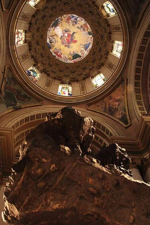 Grande meteorito rochoso e irregular sob cúpula majestosa com afresco central, vitrais coloridos e ornamentos dourados.