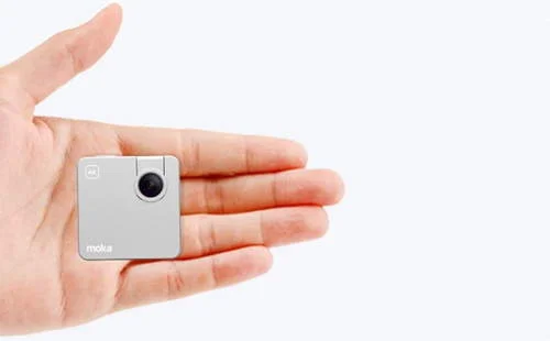 Mini câmera de ação Moka prateada, quadrada, com lente preta, na palma da mão, destacando seu formato compacto e portátil.