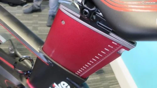 Wattbike Atom: detalhe da estrutura preta com haste de ajuste vermelha e marcações de precisão para treinamento profissional.