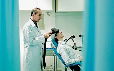 Médico aplica dispositivo de ondas magnéticas na cabeça de paciente para tratamento de enxaqueca em clínica.