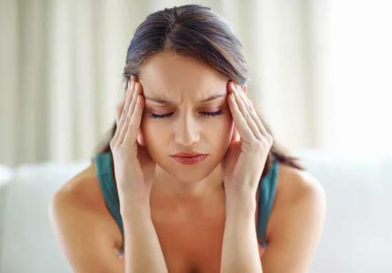Mulher com dor de cabeça e olhos fechados, pressionando têmporas; sintoma de enxaqueca.