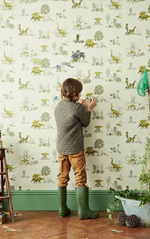 Papel de parede magnético infantil com dinossauros e cactos. Criança brinca com figuras magnéticas na parede.