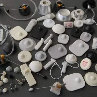 Variadas etiquetas de segurança antifurto (EAS) em branco, cinza e preto, de formatos redondos, quadrados e oblongos.