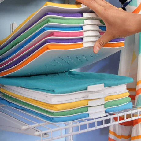 Placas organizadoras para armários, com camisetas coloridas dobradas empilhadas. Uma mão levanta uma placa de uma pilha sobre prateleira.