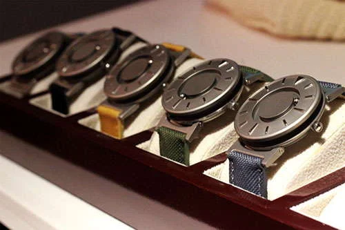 Relógios magnéticos para deficientes visuais, faces metálicas táteis com marcadores, pulseiras coloridas, em expositor de madeira.