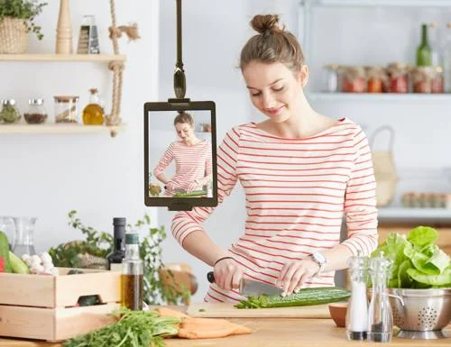 skyfloat a alça magnética para o teto segura um tablet exibindo uma mulher cozinhando, enquanto ela própria pica um pepino.