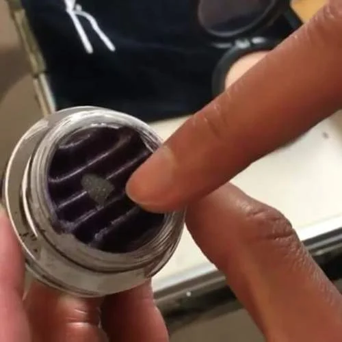 Sombras magnéticas: pote de sombra roxa escura com textura estriada e partícula cinza, sendo tocada por um dedo. Tendência do momento.