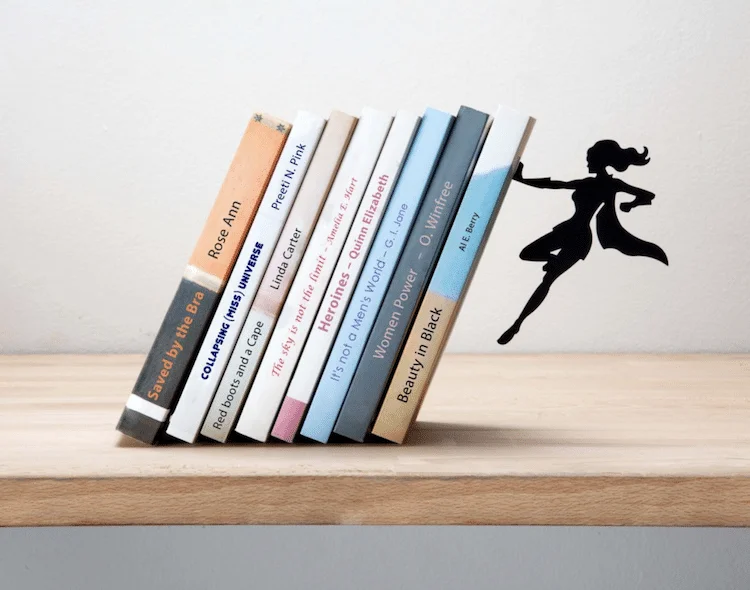 Suporte para livros com imas: oito livros inclinados na mesa, contidos por silhueta preta de heroína voando.