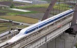 Trem bala Maglev branco e azul no Japão, em trilhos elevados de concreto, com campos e estrada ao fundo.