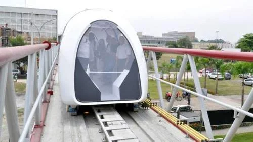 Trem de levitação magnética no Brasil. Módulo branco aerodinâmico com passageiros, em via elevada sobre trilhos e paisagem urbana.